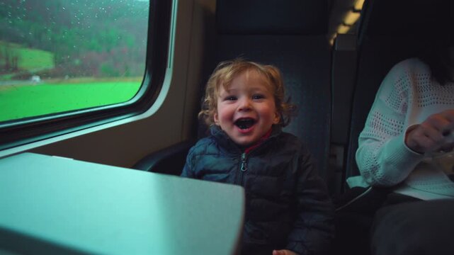 Laughing toddler sitting by train window eating blueberry snack expressing joy curiosity and playful contentment during everyday family travel
