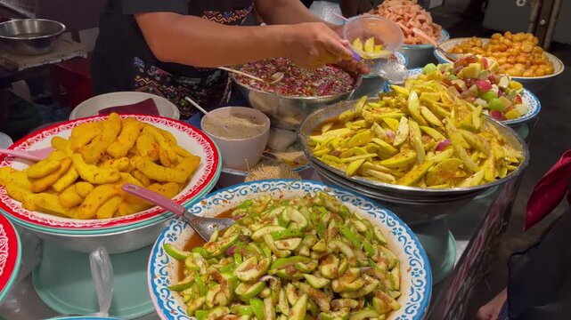Colorful Thai street food stall preparing spicy fruit salads with mango, guava, and tropical fruits, mixed fresh by hand at a local market in Thailand