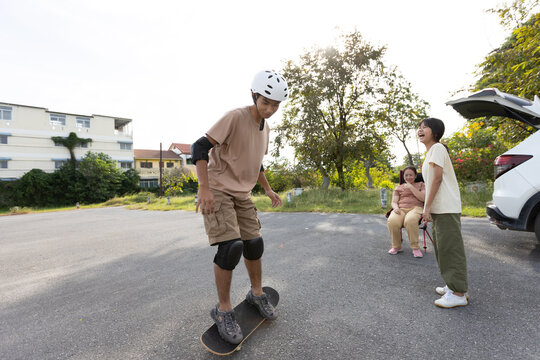 Teenage Asian Boy Balancing on Skateboard with Family Watching Outdoors