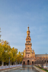Fototapeta premium The iconic North tower of the Plaza de España in Seville, Spain. The intricate Neo-Mudéjar architecture is reflected beautifully in the calm waters of the surrounding canal. 
