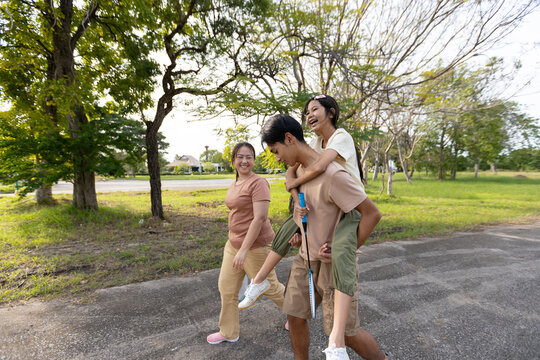 Asian Family Walking in Public Park with Brother Carrying Sister and Badminton Rackets