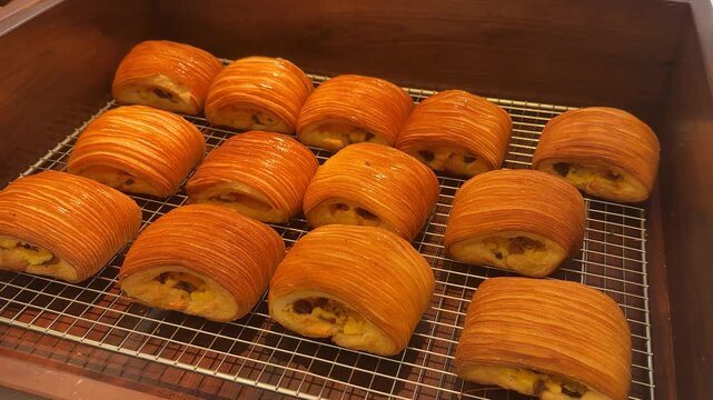 Pain au chocolat arranged on a wire rack within a wooden container, showcasing golden brown, flaky layers and rich chocolate filling, perfect for a european style breakfast or dessert