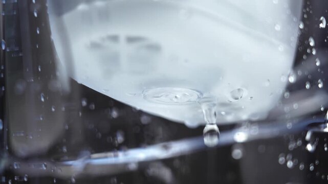 Macro view of purified water dripping from filtration cartridge inside transparent plastic pitcher. Clean liquid passing through household filtering system during purification process. 