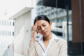 Close-up of a stressed young woman in a suit touching her forehead with eyes closed. Concept of burnout, severe headache, and workplace stress.