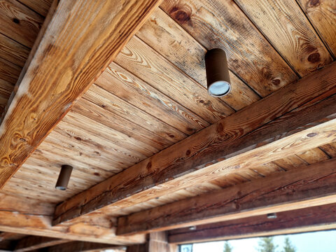 rustic ceiling structure exposed wooden beams plank ceiling. supporting structure of ceiling, which perform static aesthetic function. Modern cylindrical spotlight installed in wooden ceiling lighting