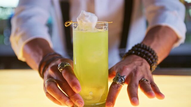 Bartender serving a green gin basil smash cocktail on a bar counter