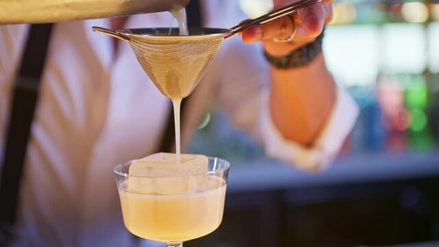 Professional bartender pouring a rum sour cocktail into glass with ice
