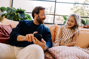 Fototapeta premium Family moment: dad and daughter on couch with phone