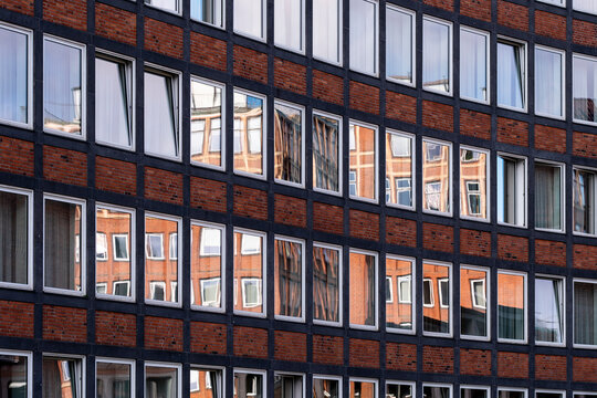 Repeating windows across a brick facade create a grid pattern of urban office architecture with clear symmetry and calm repetition