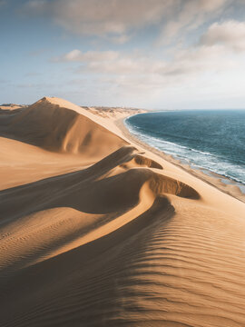 View of golden dunes meet the turquoise ocean under a vast sky, creating a stunning contrast of colors and textures, Walvis Bay, Erongo Region, Namibia.