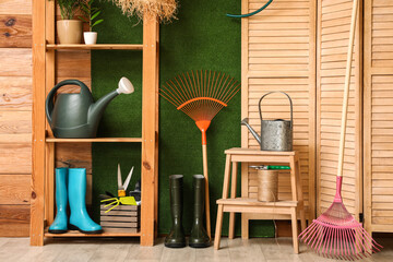 Shelving unit, folding screen and gardening supplies near wooden wall in room © Pixel-Shot