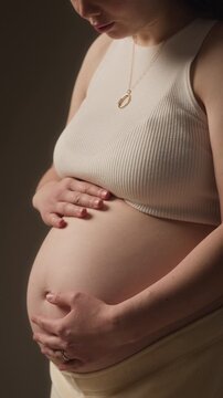 Vertical closeup portrait of expectant mother stroking her bare belly gently in soft studio light