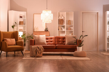 Interior of modern living room with brown sofa, armchair, shelving units and glowing lamps at evening