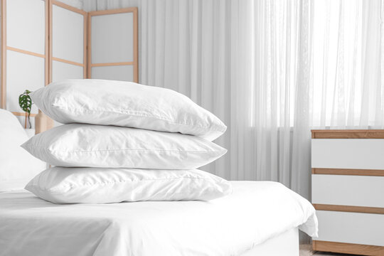 Cozy bed with white blanket and stack of soft pillows in stylish bedroom, closeup