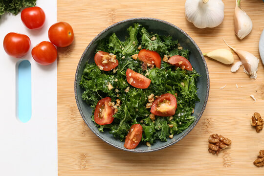 Bowl of tasty kale salad with tomatoes and garlic on wooden board