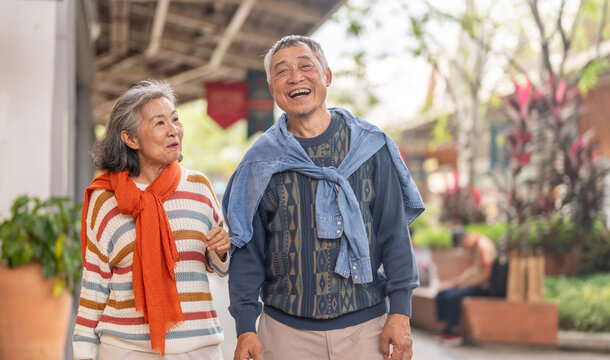 Happy senior asian couple walking and laughing together outdoors, elderly husband and wife enjoying retirement lifestyle and travel in winter, active aging, insurance and health care concept