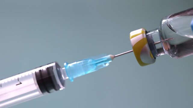 Extreme close-up of a needle piercing a vial stopper while a gloved hand pulls the syringe plunger to draw liquid medication. Medical preparation and vaccination concept.
