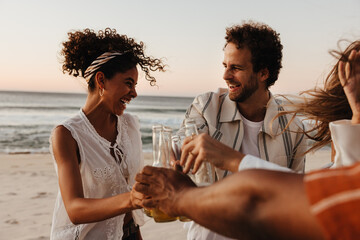 Fototapeta premium Young friends happily toasting bottles together at a beach gathering