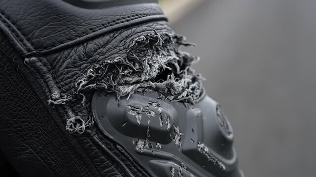 Close up of a shredded black leather motorcycle suit with damaged armor. Depicts the aftermath of a high speed crash or slide. Useful for safety awareness, insurance, or motorcycling content.