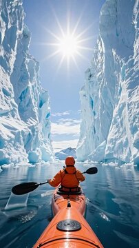 Person paddling an orange kayak between huge ice walls of an iceberg under a bright sun symbolizing exploration and nature beauty in an arctic adventure travel or global warming concept
