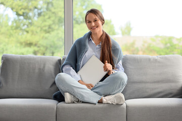 Obraz premium Young businesswoman with laptop sitting on sofa in office
