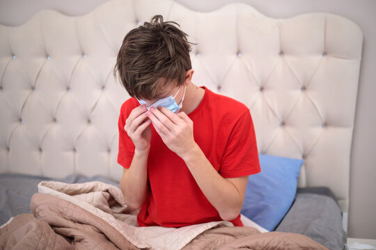 Sick teenage boy wearing medical mask and covering nose, suffering from flu or coronavirus infection, high fever, cold, cough and allergy symptoms
