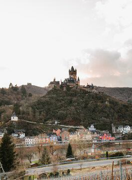 View of an imposing castle perched atop a verdant hill overlooking a quaint town nestled below against a muted sky, Cochem, Rheinland-Pfalz, Germany.