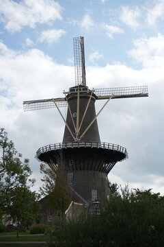 Leiden, Netherlands: View of a traditional Dutch windmill surrounded by greenery and historic buildings, set against a clear sky in a peaceful urban landscape.