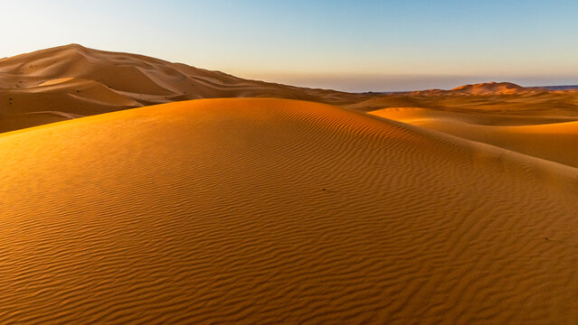 Golden sand dunes ripple across a desert landscape under a clear sky at sunset. Mezouga,Sahara desert,Morocco