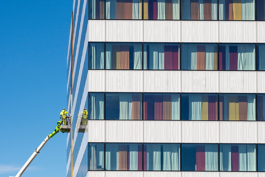Modern building facade windows under blue sky with worker cleaning from lift adding bold color to urban architecture maintenance scene