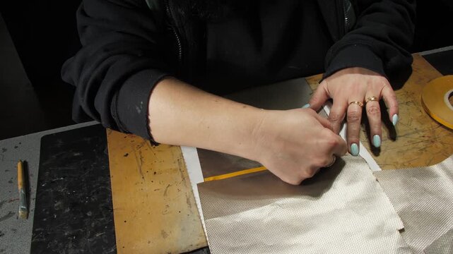 Seamstress removes adhesive tape from lining fabric elements at workplace closeup. Female worker prepares inner covering in atelier
