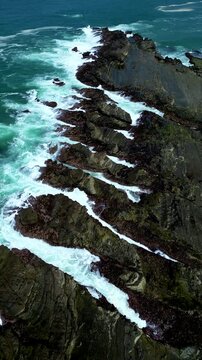 Vertical drone shot highlighting rugged rock patterns shaped by constant ocean flow at Karang Taraje Beach, Indonesia. Detailed natural textures and turquoise water movement create a striking seascape