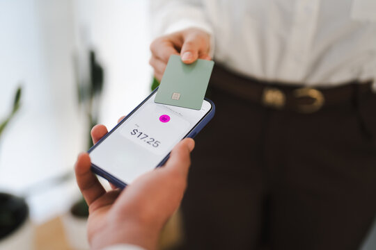 A person holds a smartphone displaying a payment amount of $17.25, while another person presents a card to complete the transaction.