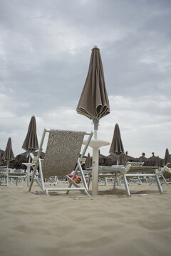 Chair and umbrella stand on a quiet beach under a cloudy sky, with soft sand stretching toward the calm sea, creating a peaceful and serene atmosphere.