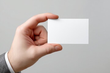 Obraz premium Hand holding a blank white business card against a plain background