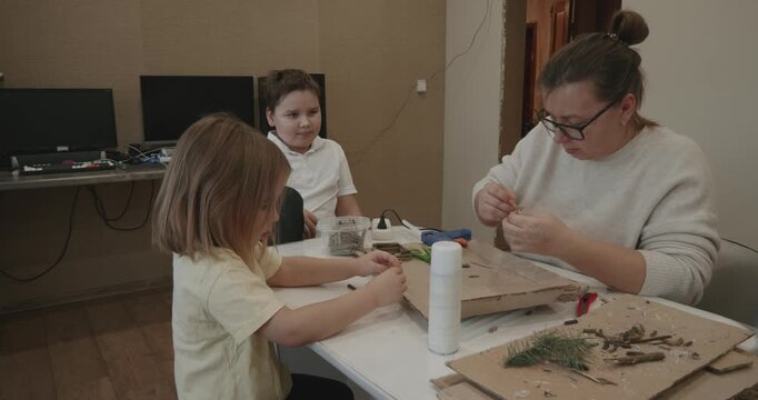 Loving family, mother, daughter, and son, spending quality time together, creating handmade decorations from natural materials like branches and pine needles during a fun and educational workshop.