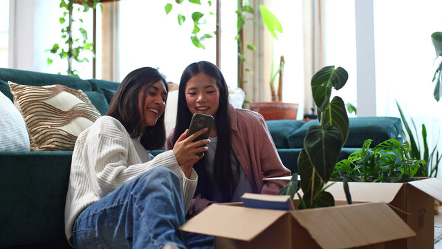 Diverse women friends smiling using phone during house relocation
