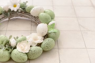 Obraz premium Easter wreath with pastel speckled eggs, white flowers and green butterfly on light rustic wooden background with copy space