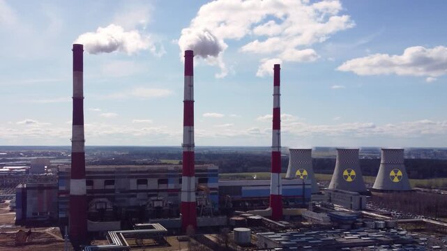 Aerial view of an industrial power plant with tall smokestacks releasing steam into the sky. Large energy facility with cooling towers marked by radioactive warning symbols in the background, 4k.