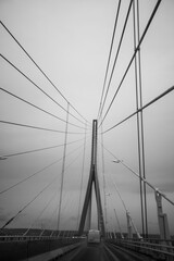 Fototapeta premium Monochrome view of a cable stayed bridge with vehicles on a wet road, dramatic architectural perspective and moody travel concept.