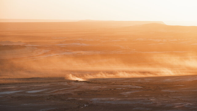 View of a desolate expanse where dust devils dance under a hazy sky, painting the scene in shades of orange and brown, Kyzylkup, Mangystau Region, Kazakhstan.