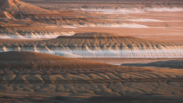 View of layered rock formations sculpted by time and elements in a majestic display of earth's artistry, bathed in warm light, Kyzylkup, Kazakhstan.