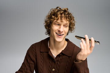 Handsome young man in stylish fashion smiling while holding a smartphone in a modern setting