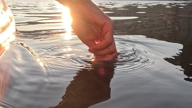 Hand, water, ripples, creating tranquil circles in calm lake during beautiful golden sunset, peaceful nature connection