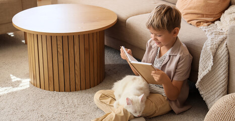 Naklejka premium Little boy with cute cat reading book at home