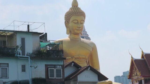 Big Seated Buddha Statue at Wat Paknam Phasi Charoen temple in Bangkok city, Thailand. Giant golden buddha statue rising above city buildings and temple rooftops. Travel and tourism in Asia