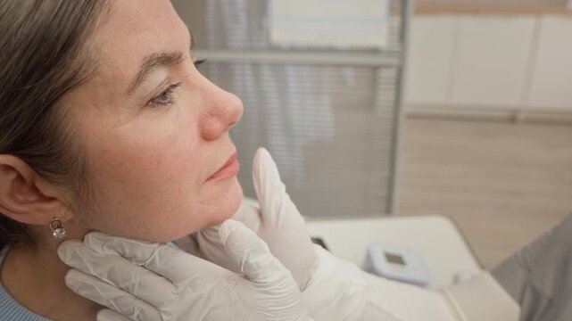 Closeup of Black female doctor wearing protective gloves preparing performing careful and precise neck gland and lymph node examination in clean modern clinic setting