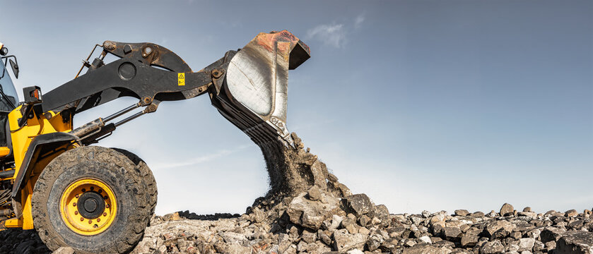 Construction equipment, such as a loader or bulldozer, lifts rocks and dumps them onto a pile at a construction site. Earthworks are used to form and level the construction site