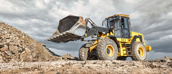A yellow loader or bulldozer lifts earth at a construction site. Earthmoving work in construction