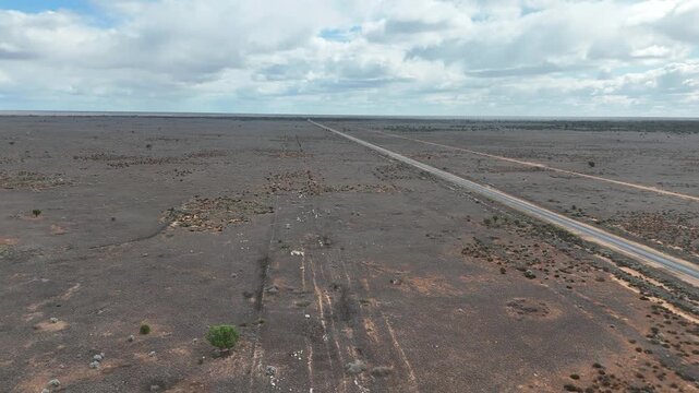 Aerial drone view over a straight road cutting through dry, sparse outback wilderness toward the distant horizon in Australia